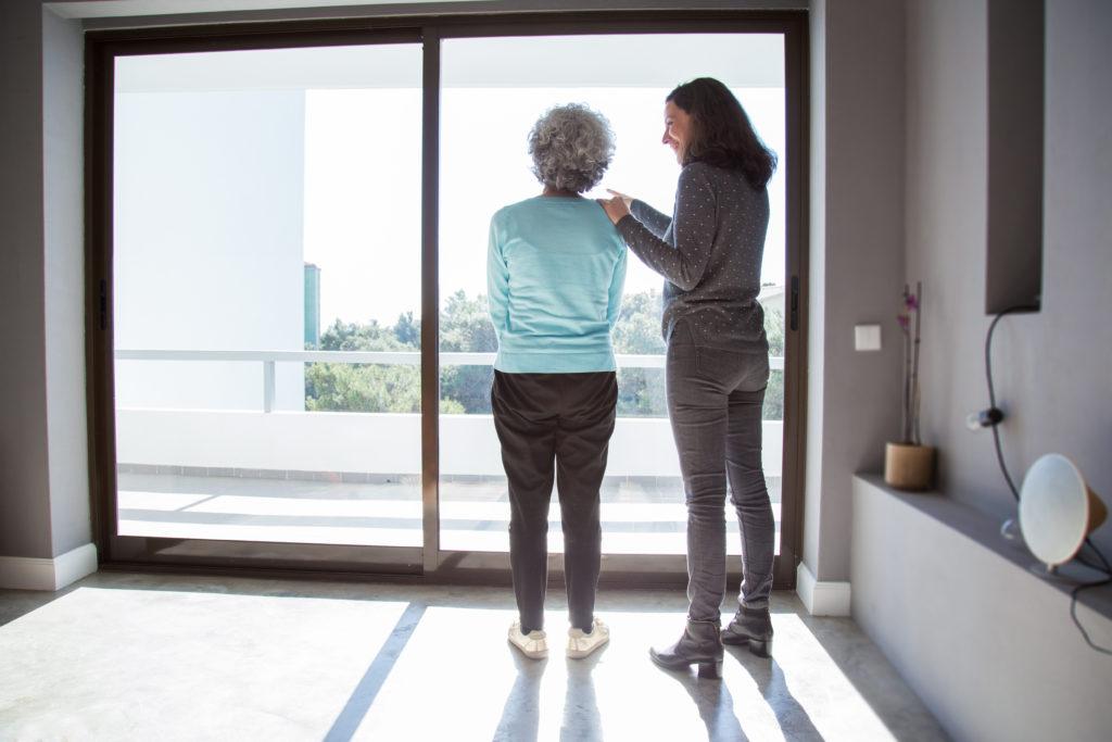 Caregiver and grandmother standing by window