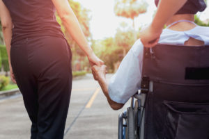 Woman holding the hand of a person being pushed in a wheelchair