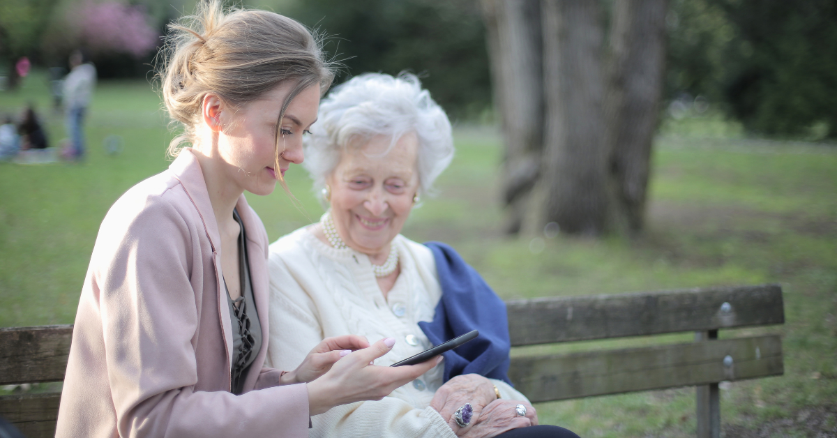 A family caregiver sitting next to her elderly mother on a park bench